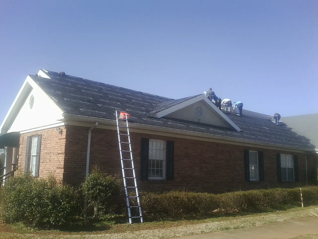 Crew tearing shingles off a brick ranch roof with a ladder set — Metal Roof Repair work by our crew in North Reading