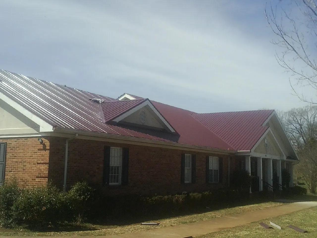 Red metal roof with gabled entries on a long brick building, from a Hail Damage Roof Repair job in North Reading