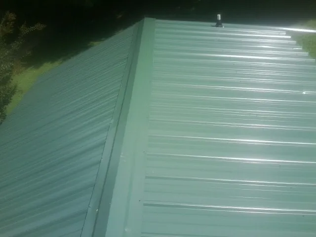 New green metal panels meeting at the ridge of a roof — Flat Roof Repair work by our crew in North Reading