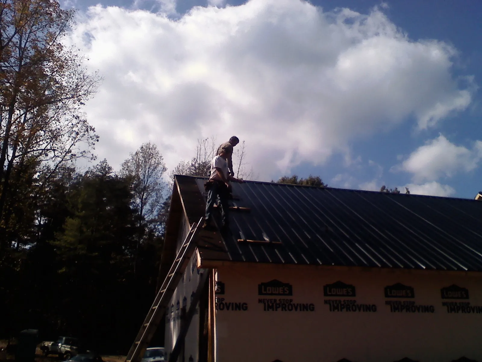 Roofer fastening dark metal panels high against a cloudy sky, from a Roof Inspection job in North Reading
